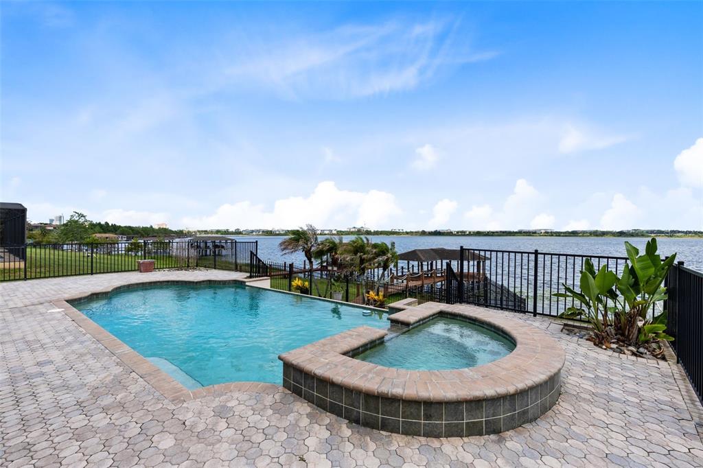 An infinity-edge swimming pool overlooks a lake with docks and a black metal fence — 10273 COVE LAKE DRIVE, ORLANDO, FL