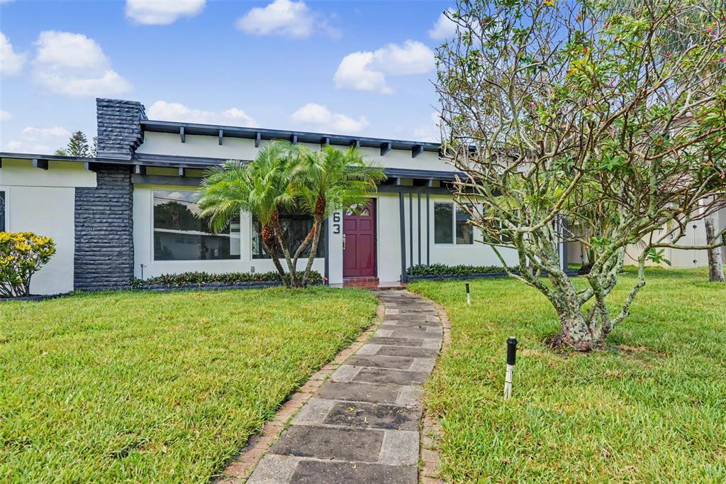 A single-story house with a stone chimney, a red front door, and a stone walkway — 63 PALM BOULEVARD, DUNEDIN, FL