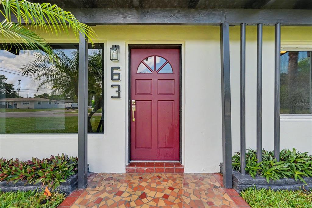 A red front door with a semi-circular window sits beneath a covered entryway — 63 PALM BOULEVARD, DUNEDIN, FL