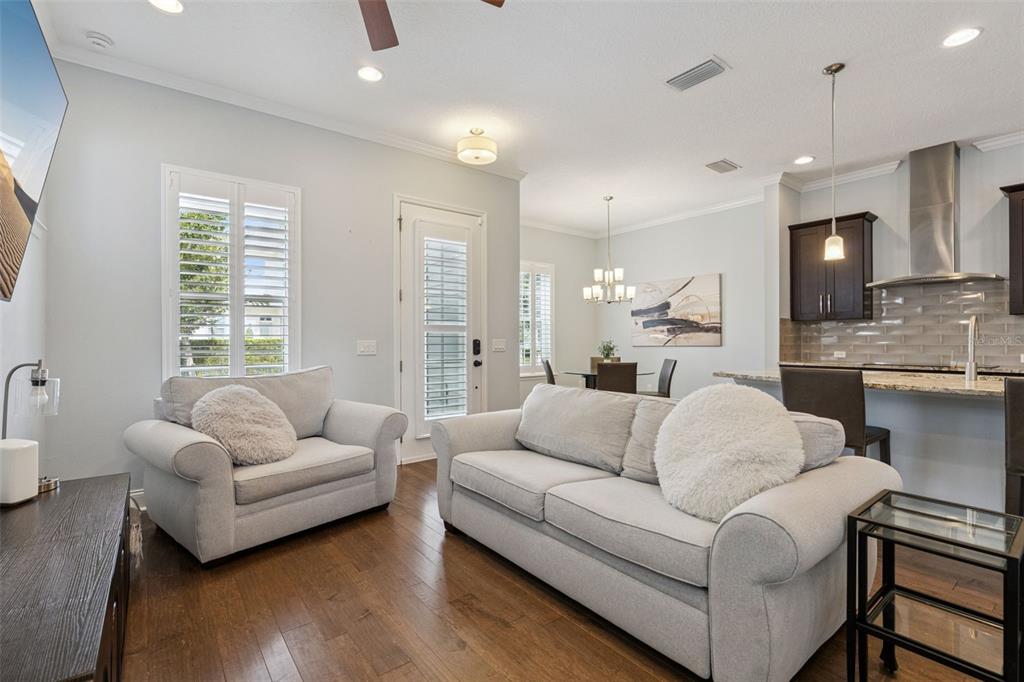 A living room with light gray furniture, hardwood floors, and an open kitchen in the background — 1589 RESOLUTE STREET, CELEBRATION, FL