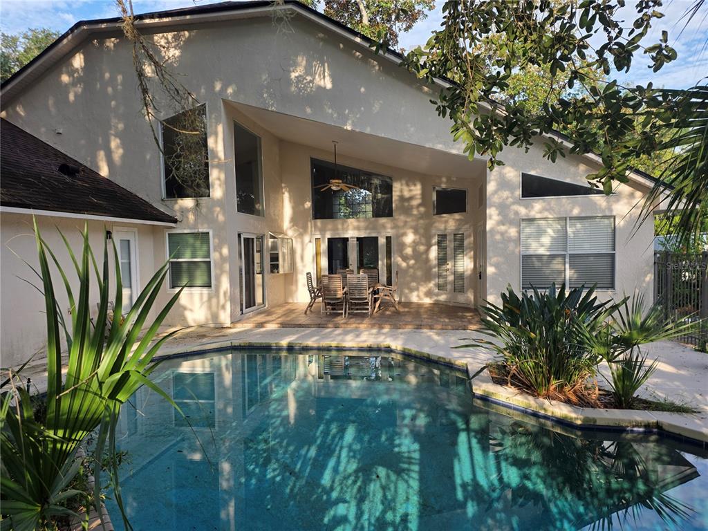 A swimming pool sits in front of a two-story house with a covered patio area — 1924 AYRSHIER PLACE, OVIEDO, FL