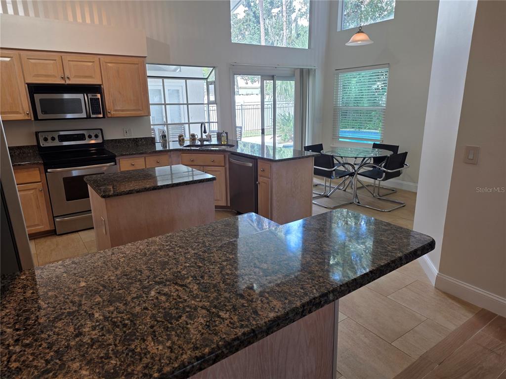 A kitchen features granite countertops, light wood cabinets, stainless steel appliances, and a dining area — 1924 AYRSHIER PLACE, OVIEDO, FL