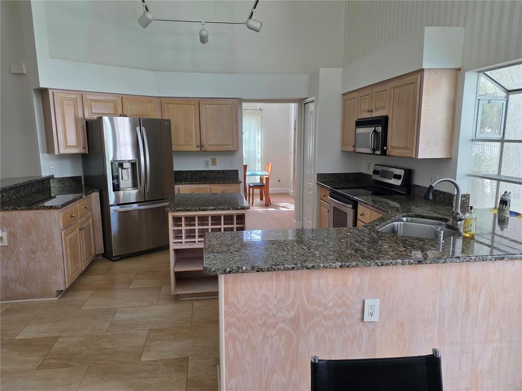 A kitchen features light wood cabinets, granite countertops, stainless steel appliances, and tile flooring — 1924 AYRSHIER PLACE, OVIEDO, FL