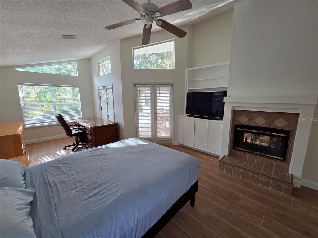 A bedroom features a bed, desk, fireplace, built-in shelving, and glass doors leading outside — 1924 AYRSHIER PLACE, OVIEDO, FL