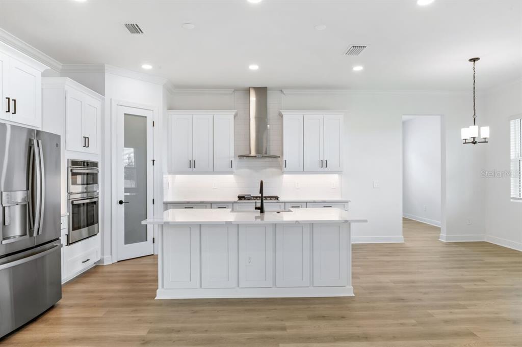 A modern kitchen features white cabinetry, a central island, stainless steel appliances, and light flooring — 17536 MACARTHUR LOOP, VENICE, FL