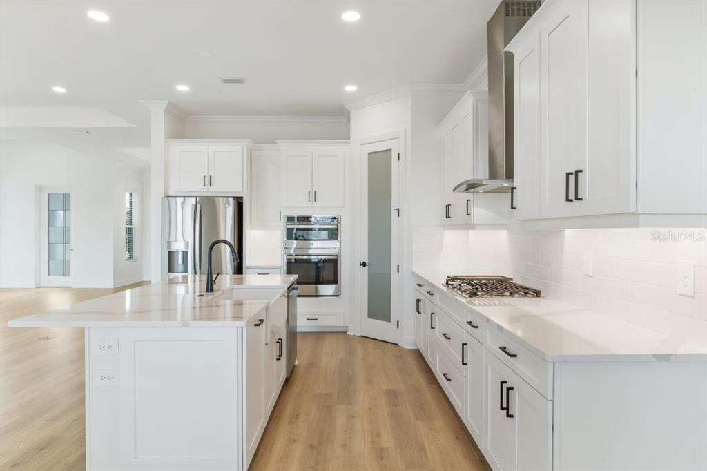 A modern kitchen features white cabinets, a large island, stainless steel appliances, and wood flooring — 17536 MACARTHUR LOOP, VENICE, FL