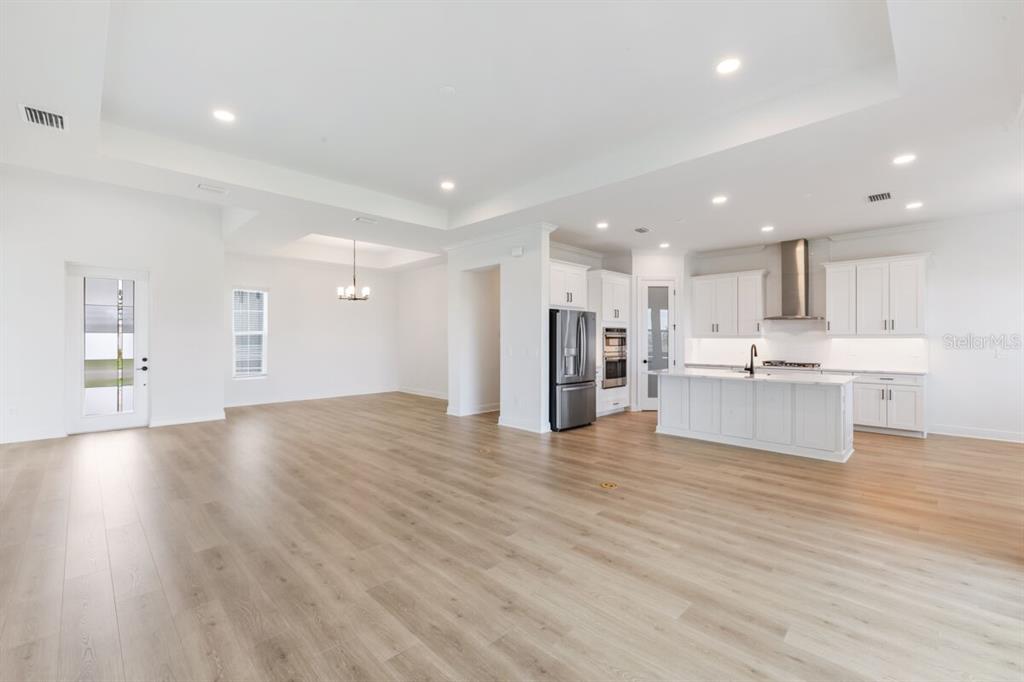 This open-concept living area features light wood flooring, white cabinetry, and a kitchen island — 17536 MACARTHUR LOOP, VENICE, FL