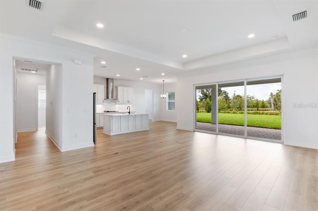An open-concept living area features light wood flooring, a white kitchen, and sliding glass doors — 17536 MACARTHUR LOOP, VENICE, FL