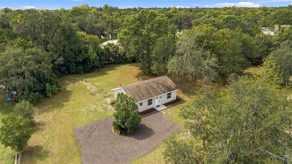 An aerial view shows a small, light-colored house situated on a large, tree-lined grassy lot — 15210 LANCER ROAD, SPRING HILL, FL