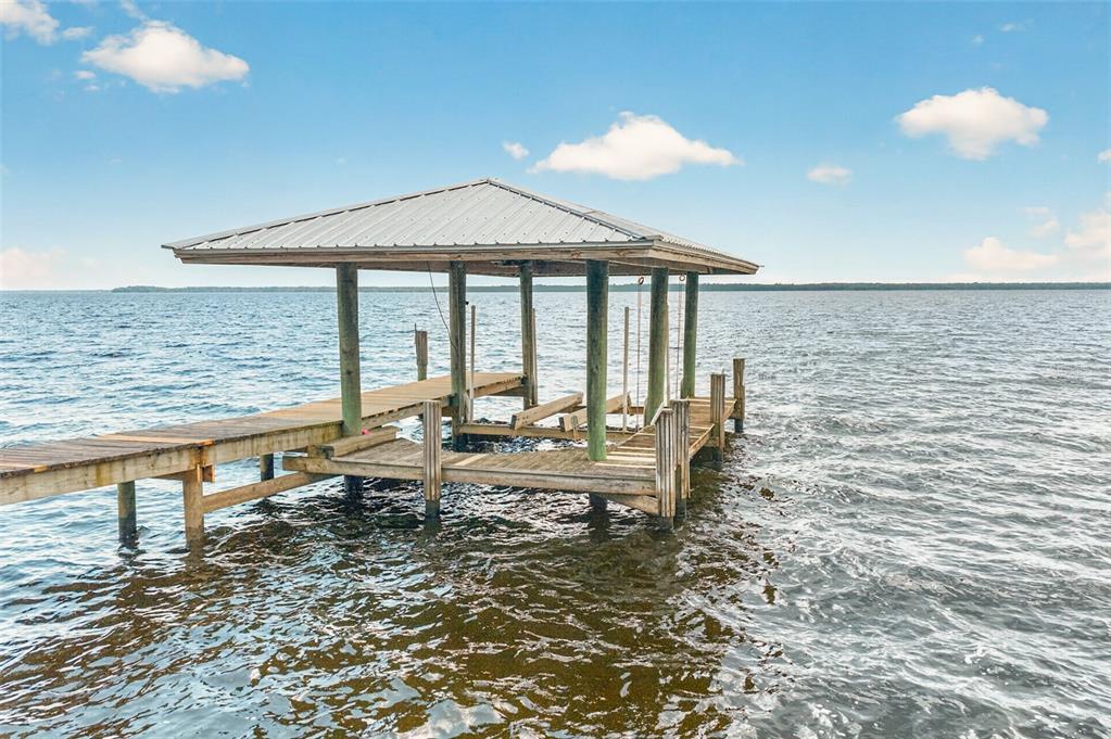 A wooden dock with a covered boat slip extends into a large, calm lake — 6373 JACK WRIGHT ISLAND ROAD, ST AUGUSTINE, FL