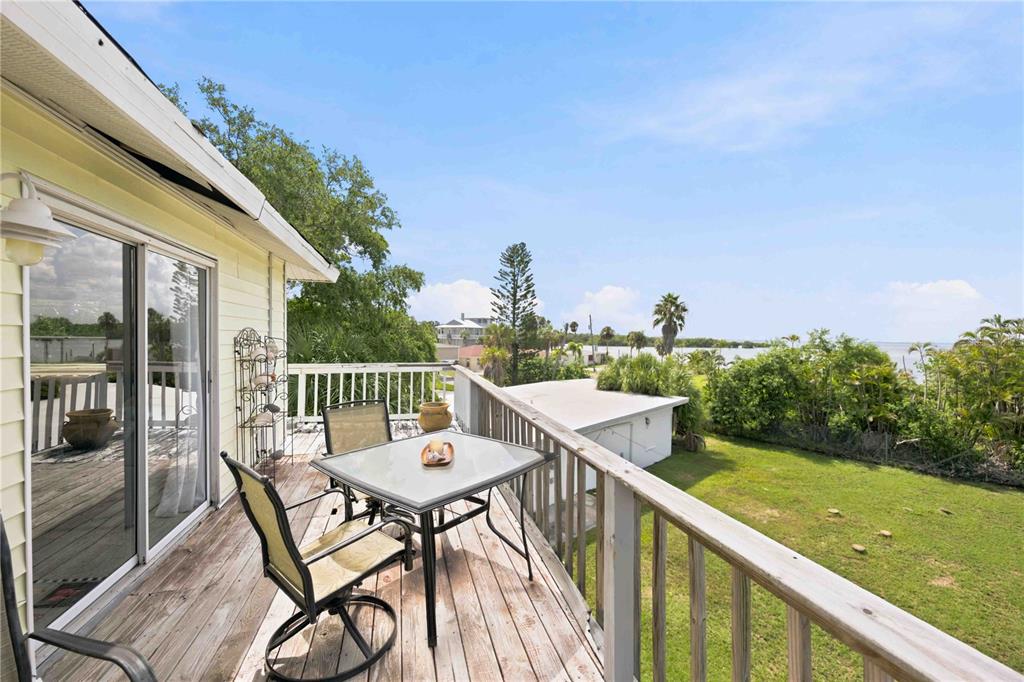 A wooden deck with a table and chairs overlooks a grassy yard and the water — 6904 22ND STREET W, BRADENTON, FL