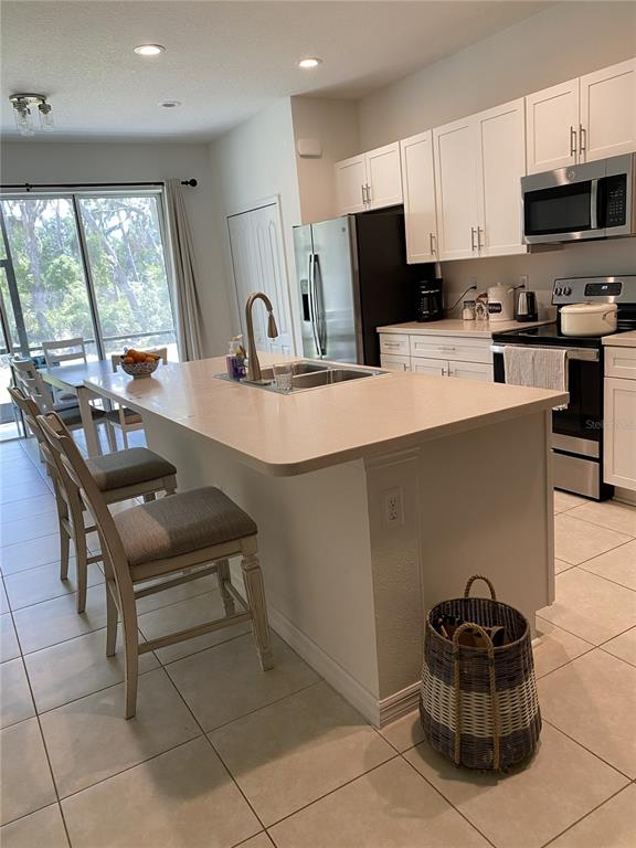 A kitchen features a central island with bar seating, white cabinetry, and stainless steel appliances — 8443 CANYON CREEK TRAIL, PARRISH, FL