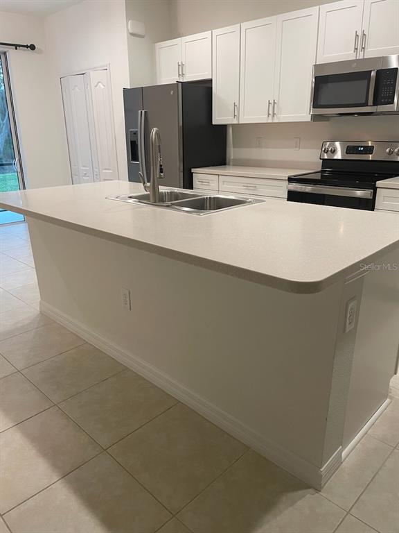 A kitchen features white cabinets, a large island with a sink, and stainless steel appliances — 8443 CANYON CREEK TRAIL, PARRISH, FL