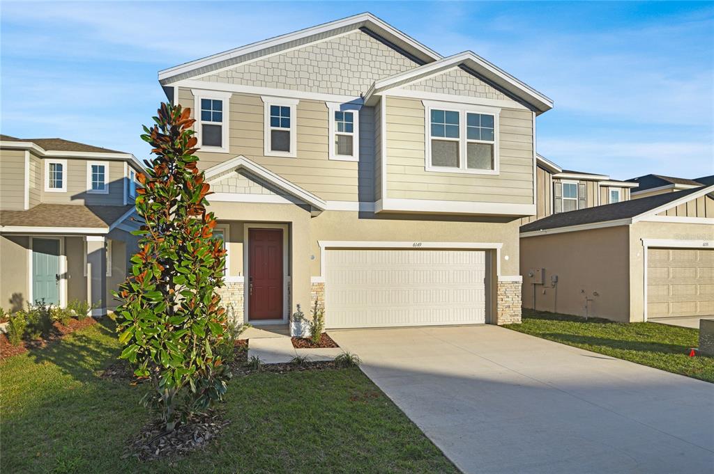 A two-story suburban house with beige siding, a red front door, and a two-car garage — 6149 SW 64TH TERRACE, OCALA, FL