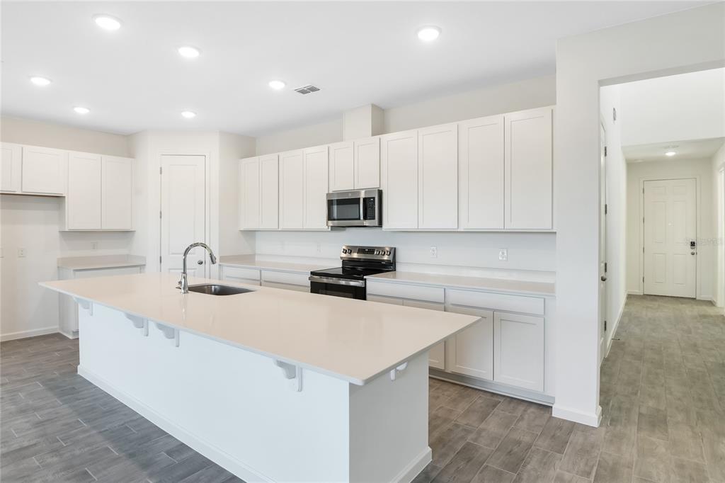 A modern kitchen features white cabinetry, a large island with a sink, and gray flooring — 6149 SW 64TH TERRACE, OCALA, FL
