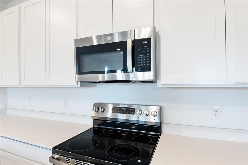 A stainless steel microwave and electric range are installed between white kitchen cabinets — 6149 SW 64TH TERRACE, OCALA, FL