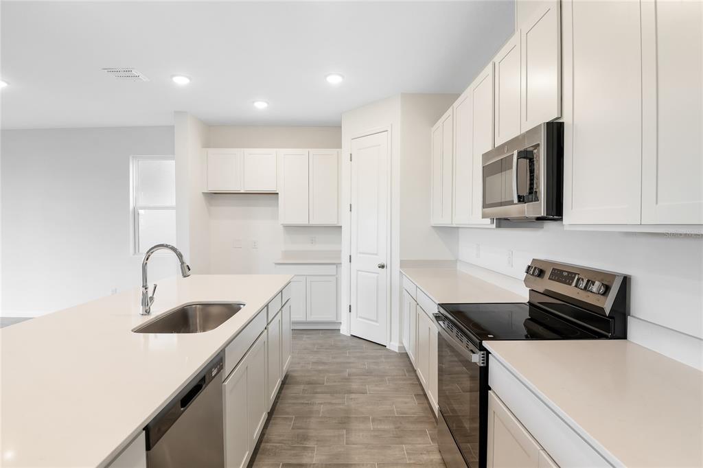 A modern kitchen features white cabinets, quartz countertops, stainless steel appliances, and a center island — 6149 SW 64TH TERRACE, OCALA, FL