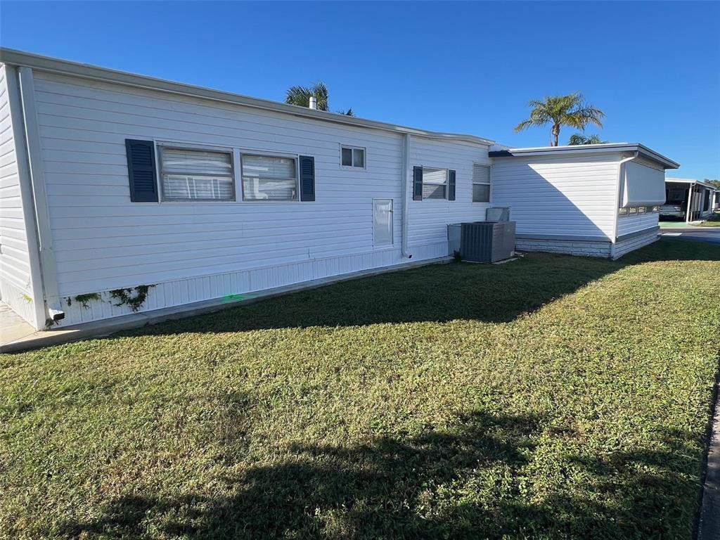 The exterior of a white mobile home features horizontal siding, blue shutters, and a lawn — 11300 124TH AVENUE UNIT 150, LARGO, FL
