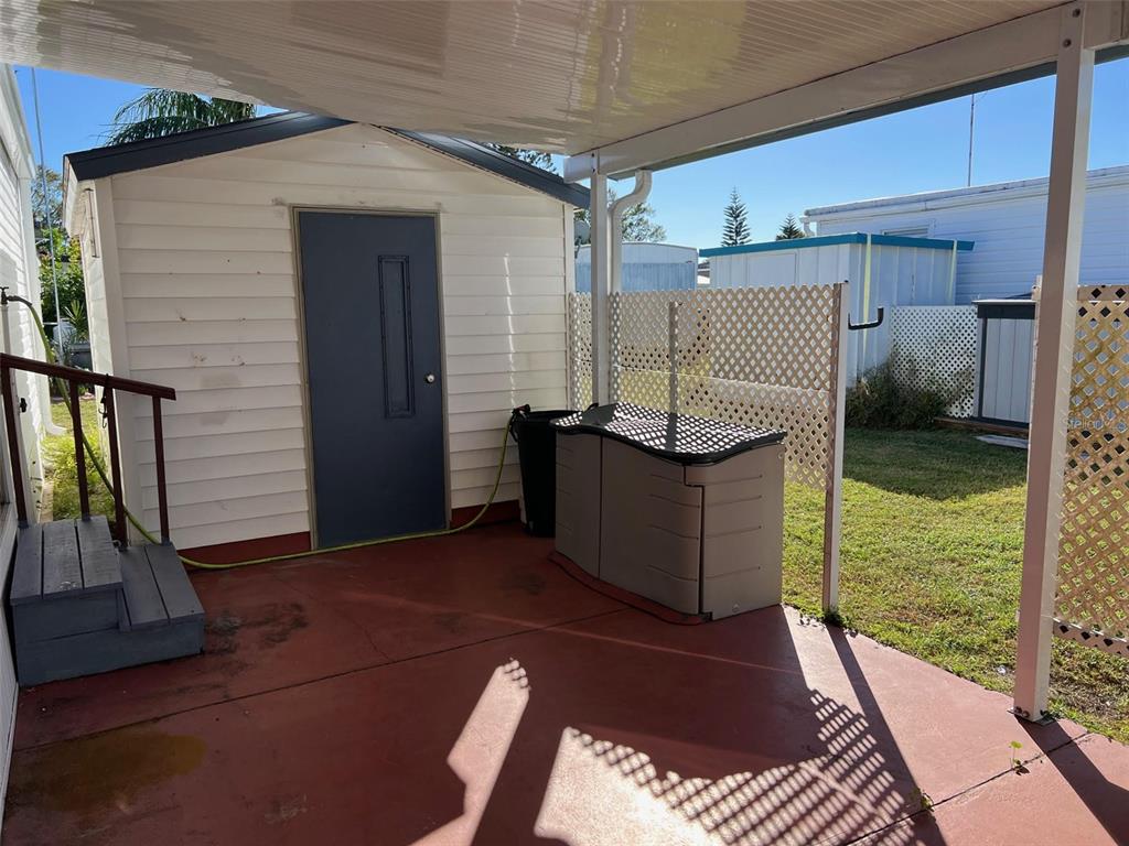 A covered patio with a shed, storage bin, and lattice fencing in a backyard setting — 11300 124TH AVENUE UNIT 150, LARGO, FL