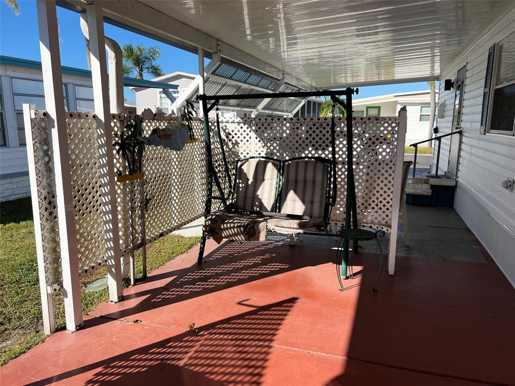 A covered patio features a metal porch swing, lattice privacy screens, and painted concrete flooring — 11300 124TH AVENUE UNIT 150, LARGO, FL