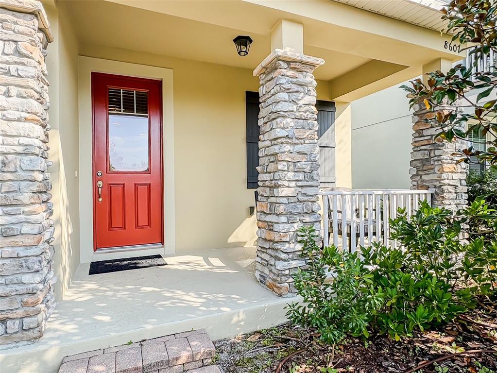 A covered porch features a red door, two striped chairs, and a stone pillar — 8607 RANDAL PARK BOULEVARD, ORLANDO, FL