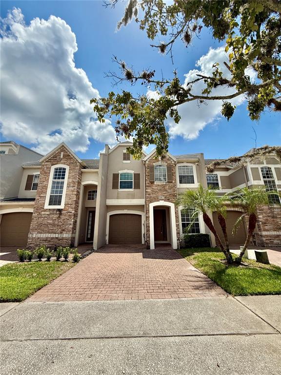 A two-story townhouse with a stone facade, brick driveway, and an attached garage — 547 TERRACE SPRING DRIVE, ORLANDO, FL