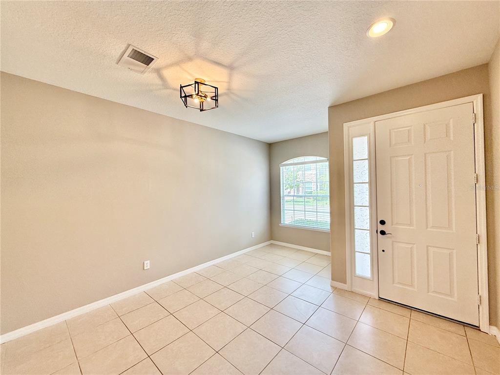 An entryway with beige walls, tile flooring, a geometric light fixture, and a white front door — 547 TERRACE SPRING DRIVE, ORLANDO, FL
