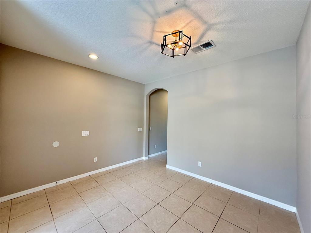 An empty room features beige walls, tile flooring, a geometric light fixture, and an arched doorway — 547 TERRACE SPRING DRIVE, ORLANDO, FL