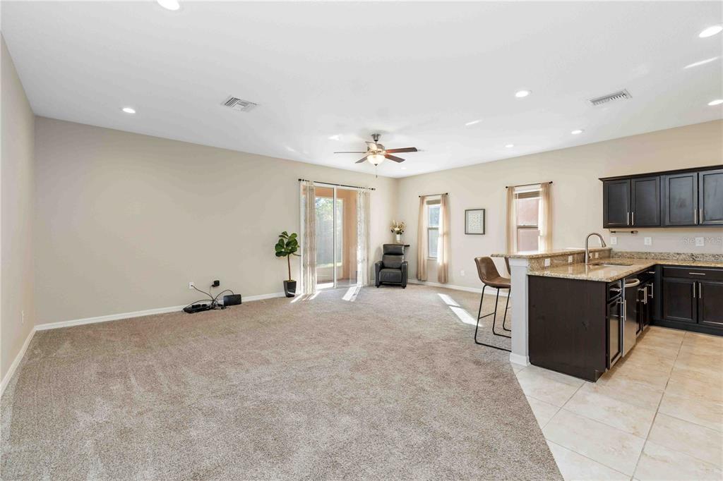 A spacious living room with beige carpet opens to a kitchen with dark cabinets — 1218 GRANTHAM DRIVE, SARASOTA, FL
