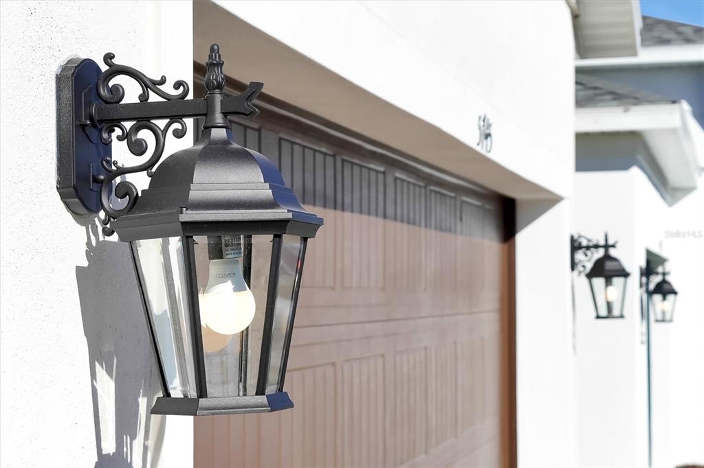 A black outdoor lantern light fixture is mounted on a white wall beside a garage — 5745 WALLIS LANE, ST CLOUD, FL