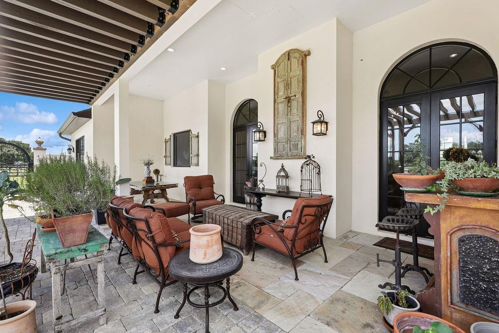 A covered patio features stone flooring, outdoor furniture, potted plants, and arched glass doors — 11408 N MAGNOLIA AVENUE, OCALA, FL