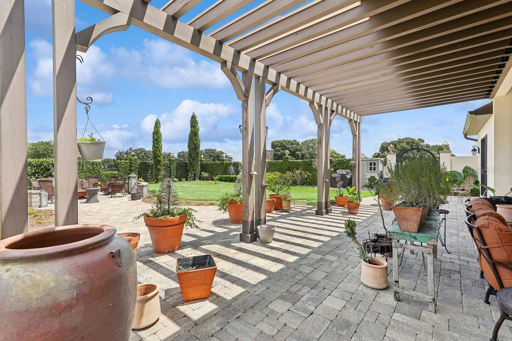 A paved patio features a wooden pergola, numerous potted plants, and a view of a lawn — 11408 N MAGNOLIA AVENUE, OCALA, FL