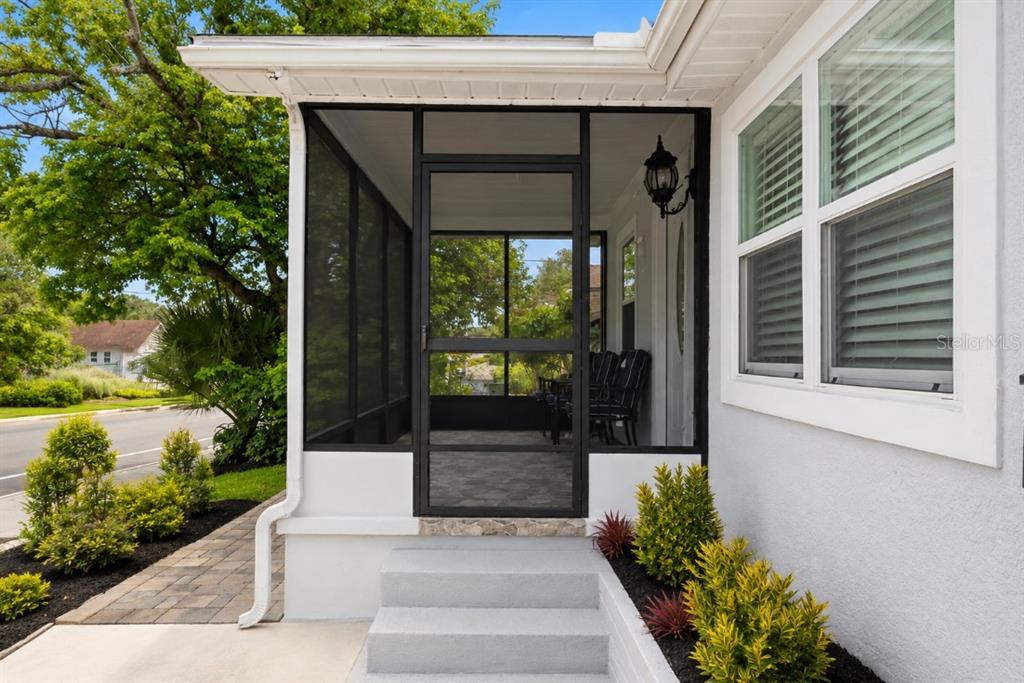 A screened-in porch with a black frame and concrete steps sits beside a white house — 8912 N 40TH STREET, TAMPA, FL