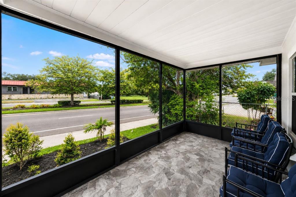 A screened-in porch with stone-look flooring and blue patio chairs overlooking a street and trees — 8912 N 40TH STREET, TAMPA, FL