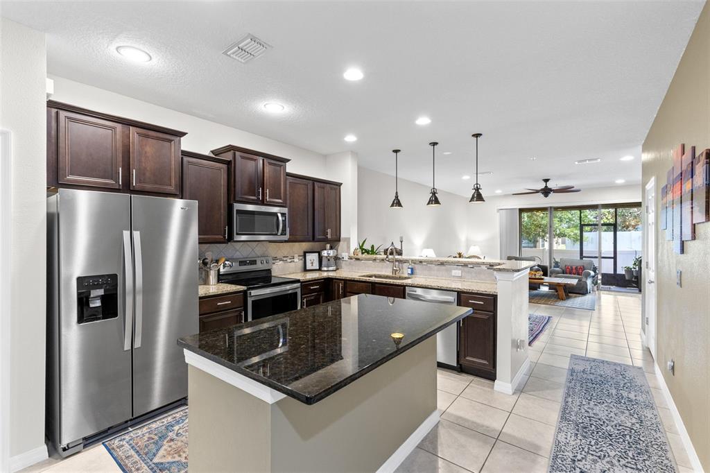 A kitchen with dark wood cabinets, granite countertops, stainless steel appliances, and a center island — 1120 PAVIA DRIVE, APOPKA, FL