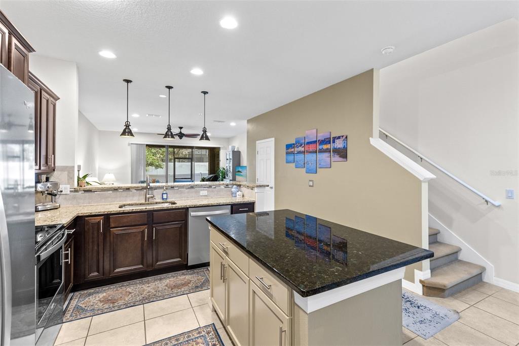 A kitchen with dark wood cabinets, a light-colored island, granite countertops, and a staircase nearby — 1120 PAVIA DRIVE, APOPKA, FL