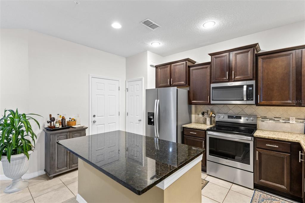 A kitchen features dark wood cabinets, granite countertops, stainless steel appliances, and a central island — 1120 PAVIA DRIVE, APOPKA, FL