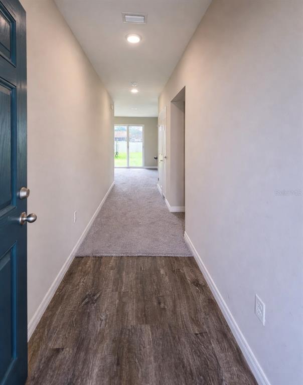 A hallway with wood-look flooring transitions into a carpeted living area with sliding glass doors — 1392 AXEL CIR, WINTER HAVEN, FL