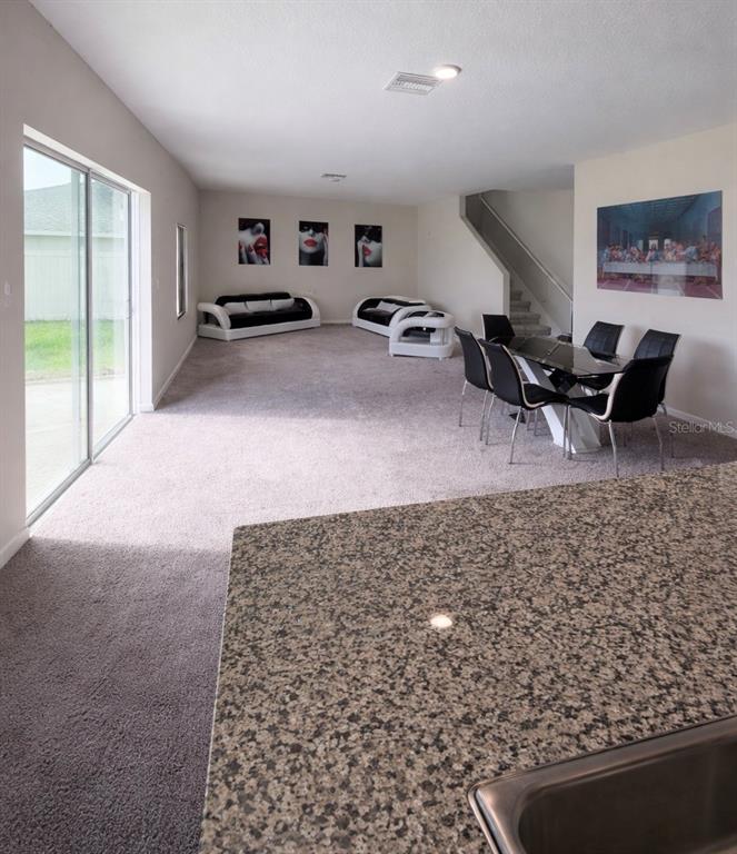 An open-concept living and dining area features carpeted flooring, modern furniture, and a granite countertop — 1392 AXEL CIR, WINTER HAVEN, FL