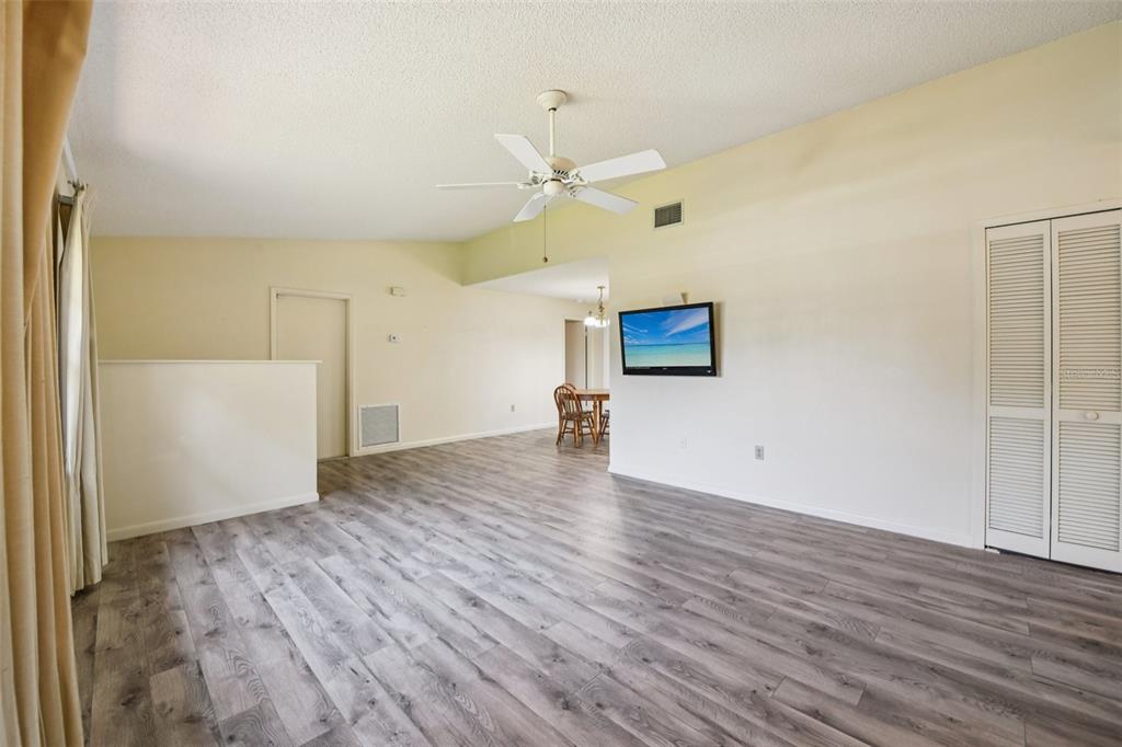 A living room with light-colored walls, gray wood-look flooring, a ceiling fan, and a television — 3826 PARAPET DRIVE, COCOA, FL