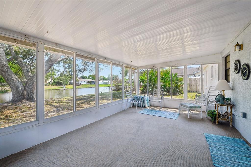 A sunroom with carpeted floors, white walls, and large windows overlooking a small pond — 3826 PARAPET DRIVE, COCOA, FL