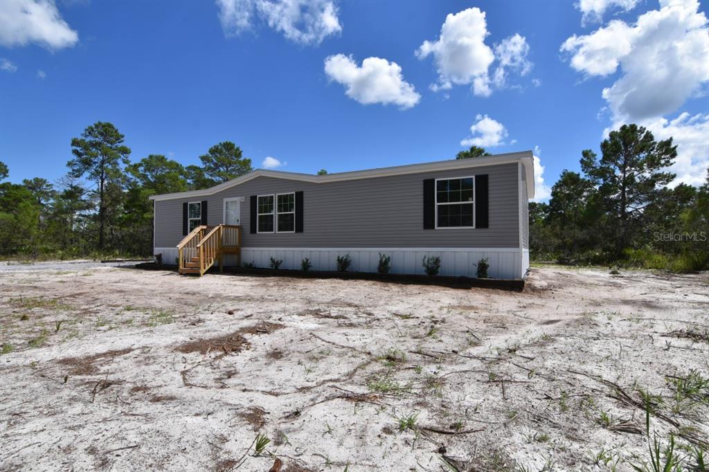 A gray manufactured home with white skirting sits on a sandy lot under a blue sky — 192 FREEDOM DRIVE, FROSTPROOF, FL