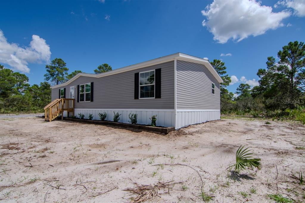 A gray manufactured home with black shutters sits on a sandy lot under blue skies — 192 FREEDOM DRIVE, FROSTPROOF, FL