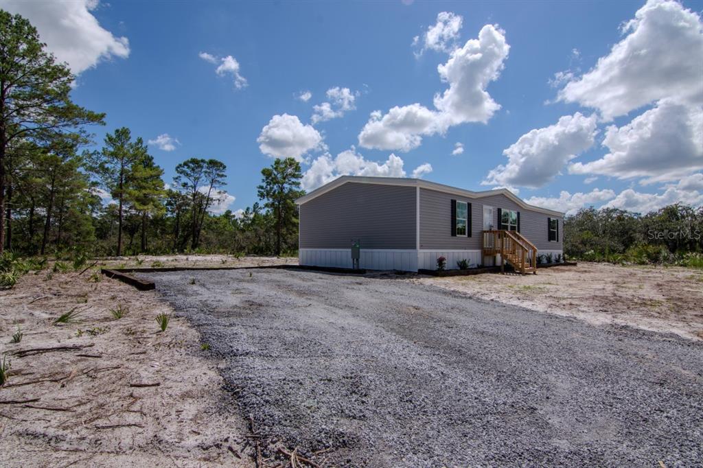 A gray manufactured home sits on a gravel driveway surrounded by trees and sandy ground — 192 FREEDOM DRIVE, FROSTPROOF, FL