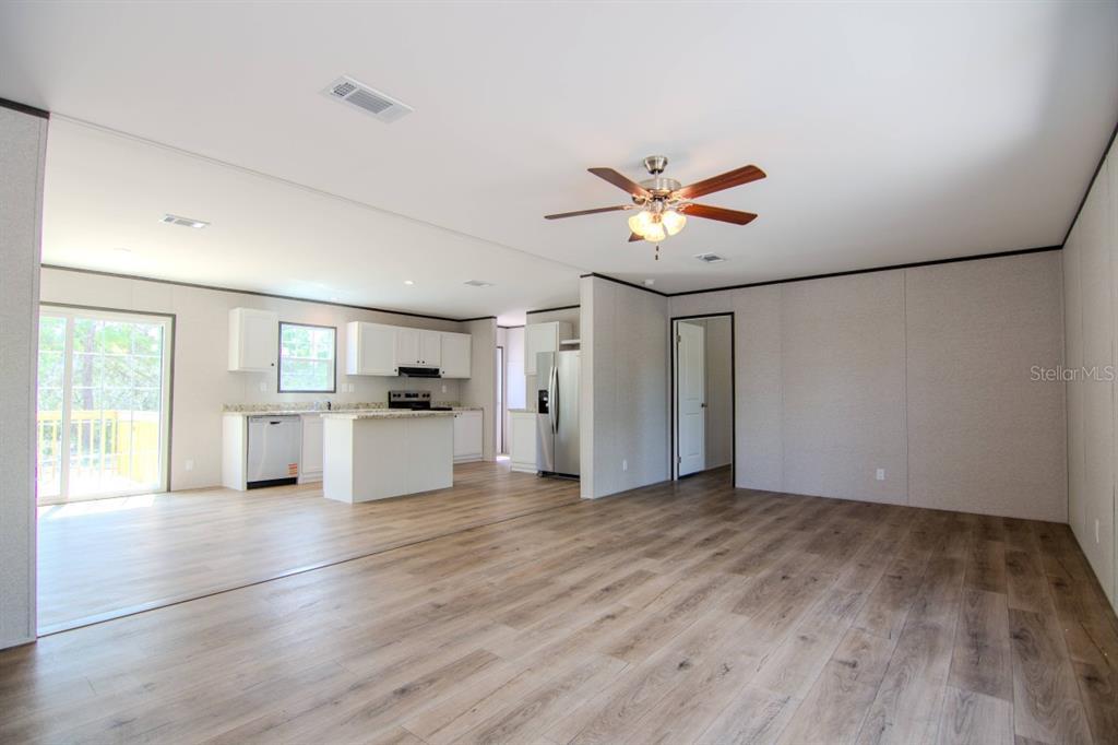 An open-concept kitchen and living area features light wood-look flooring, white cabinetry, and a ceiling fan — 192 FREEDOM DRIVE, FROSTPROOF, FL