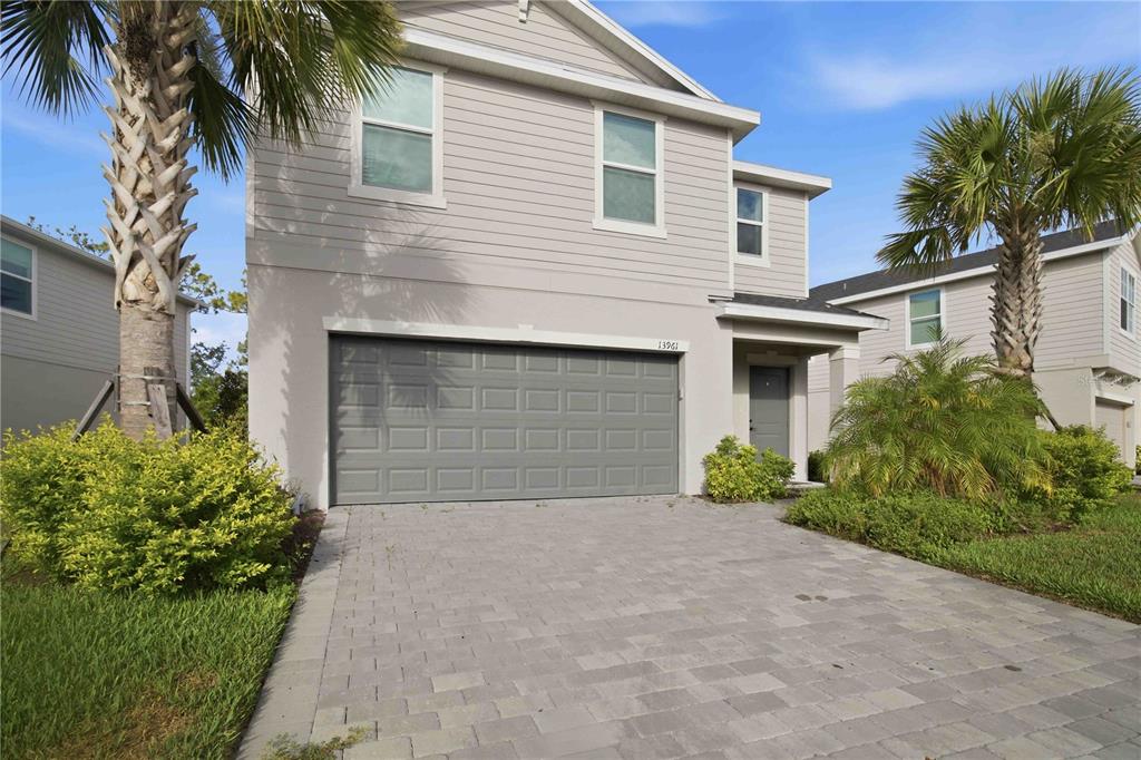 A two-story house with a gray garage door, light siding, and a paved driveway — 13961 LILAC SKY TERRACE, BRADENTON, FL