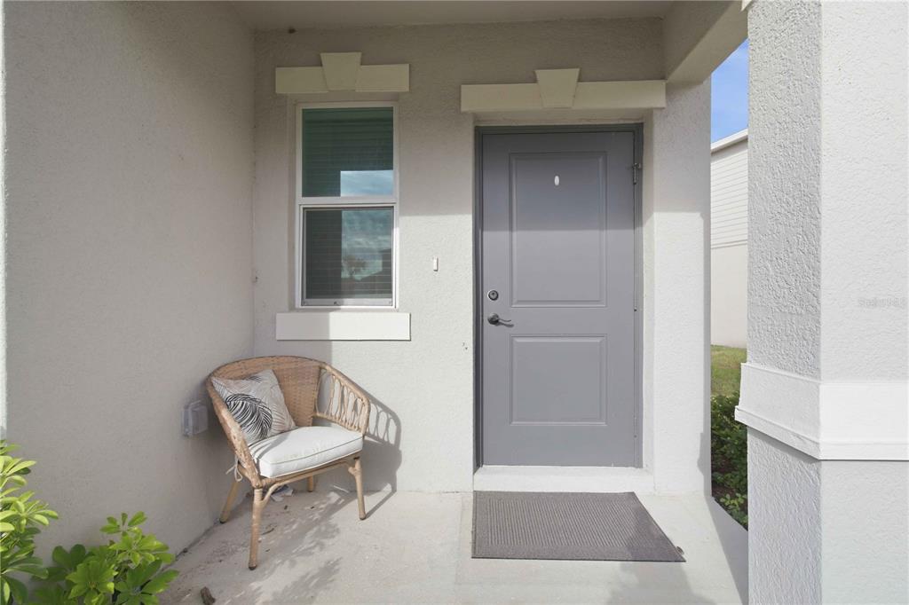 A covered front porch features a gray door, a single window, and a wicker chair — 13961 LILAC SKY TERRACE, BRADENTON, FL
