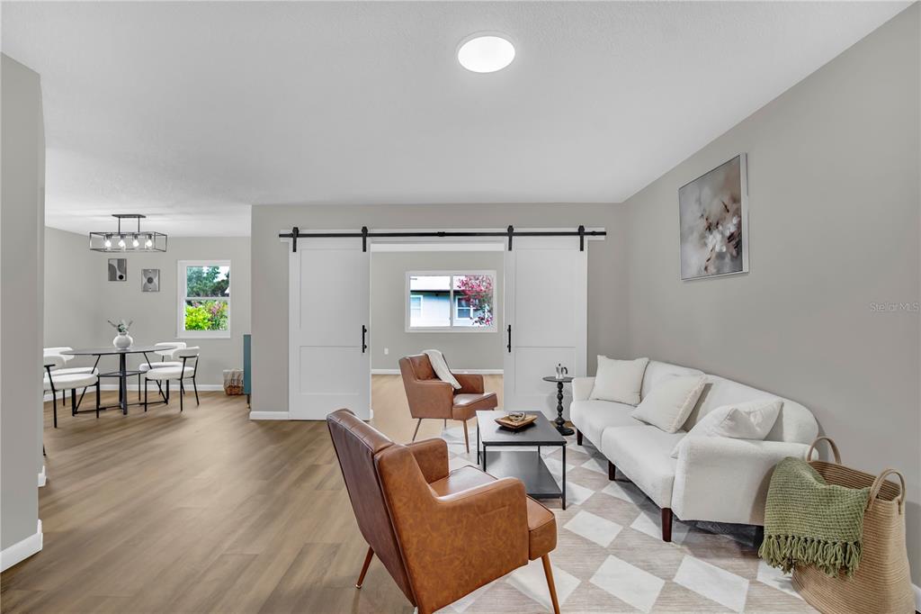 A living room with wood-look flooring, a white sofa, two leather chairs, and sliding barn doors — 2314 BONNIE VIEW COURT, LEESBURG, FL