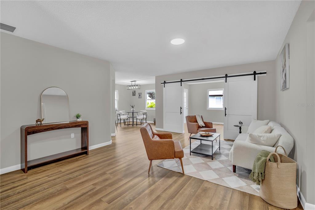 A living room with wood-look flooring, a white sofa, leather chairs, and sliding barn doors — 2314 BONNIE VIEW COURT, LEESBURG, FL