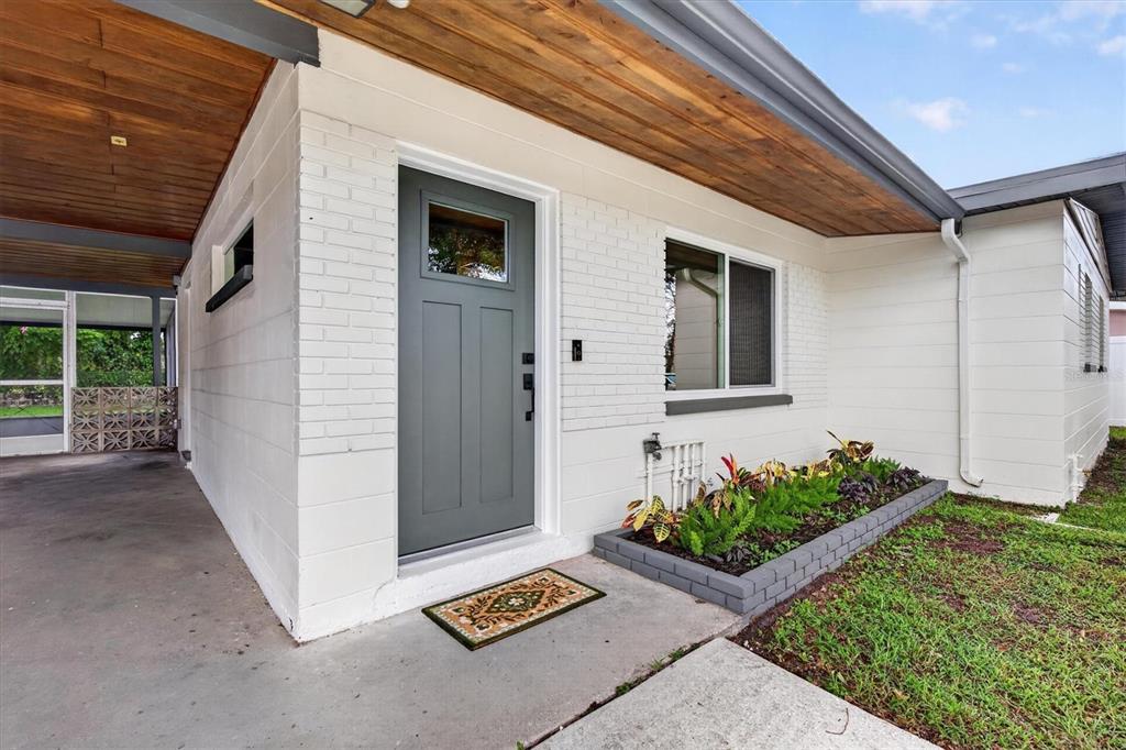 A white brick house exterior features a gray front door, wood-paneled ceiling, and garden bed — 5305 E 98TH AVENUE, TEMPLE TERRACE, FL